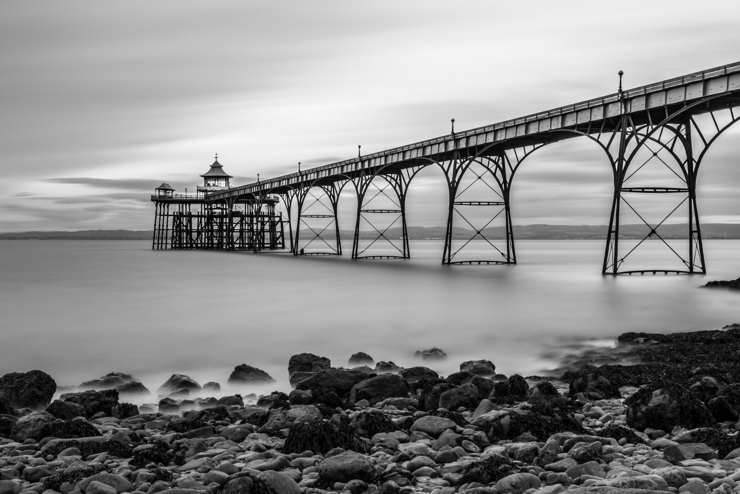 grayscale shot bridge lake stones bay cloudy day scaled